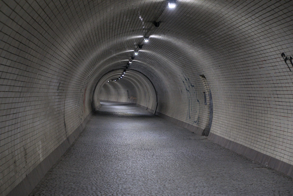inside a long tunnel with tiled walls and dim lights