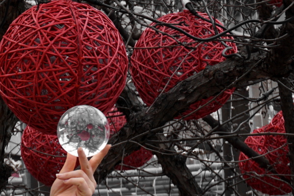 branches of a tree with large decoration balls and a hand holding a glass sphere